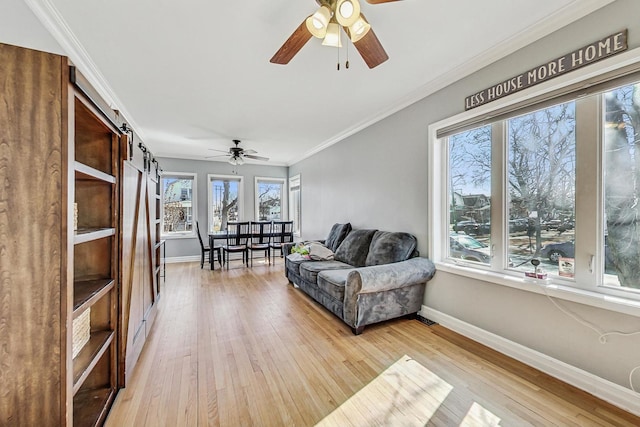 living room with crown molding, a barn door, a ceiling fan, light wood-type flooring, and baseboards