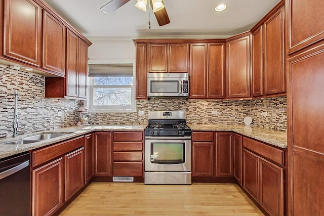 kitchen with stainless steel appliances, a sink, light wood-style floors, backsplash, and light stone countertops