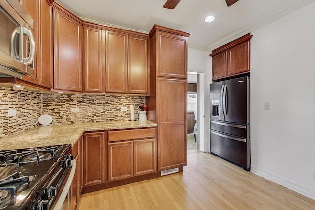 kitchen featuring ceiling fan, appliances with stainless steel finishes, ornamental molding, light wood-type flooring, and backsplash