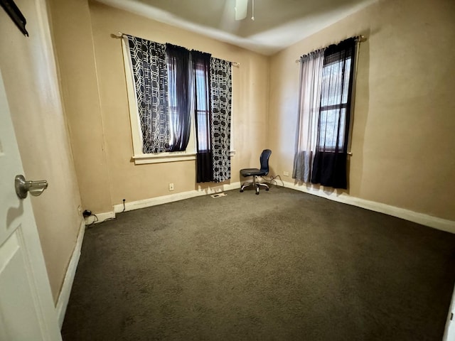 spare room featuring dark colored carpet, a ceiling fan, and baseboards