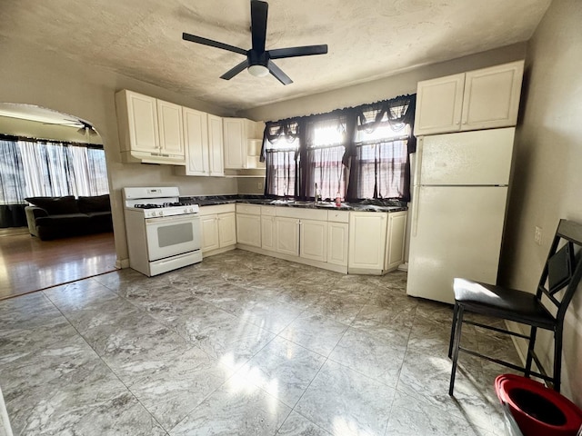 kitchen featuring white appliances, arched walkways, a ceiling fan, dark countertops, and under cabinet range hood