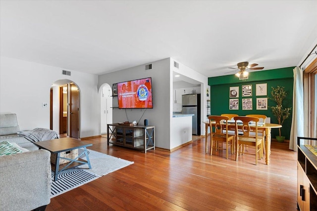 living area with a ceiling fan, visible vents, arched walkways, and hardwood / wood-style floors