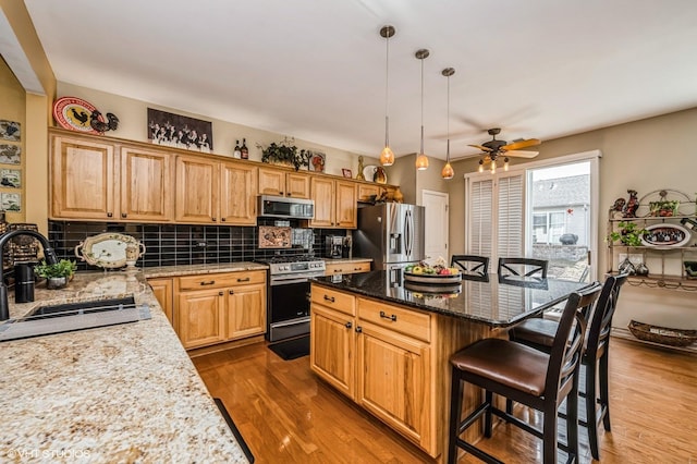 kitchen with a breakfast bar, a sink, backsplash, wood finished floors, and appliances with stainless steel finishes