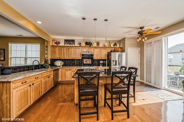 kitchen featuring a sink, backsplash, stainless steel appliances, wood-type flooring, and stone counters