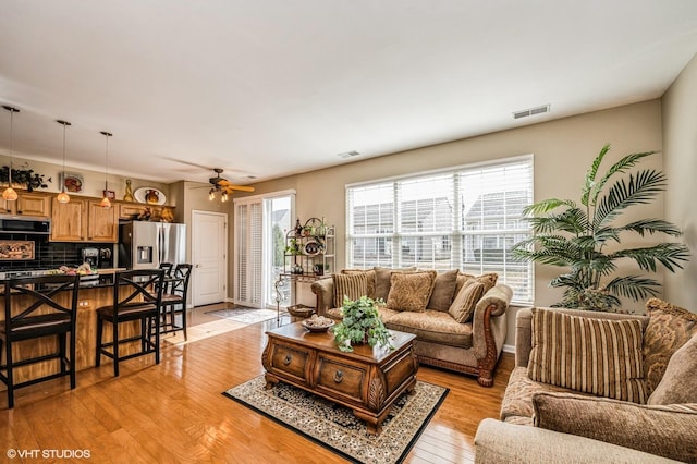 living room featuring light wood-style flooring, visible vents, and ceiling fan