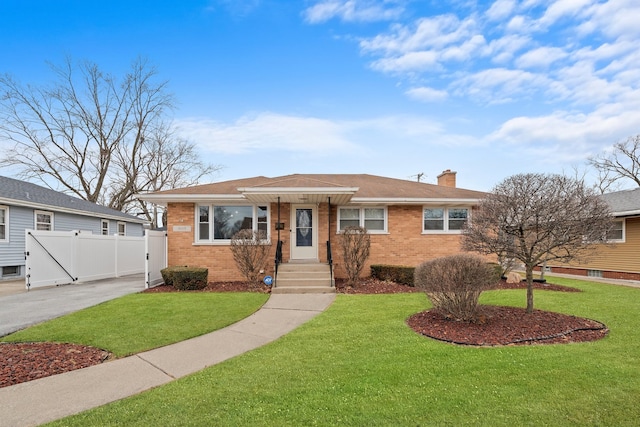 view of front facade with brick siding, fence, driveway, a front lawn, and a chimney