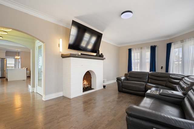 living area with baseboards, ornamental molding, a fireplace, wood finished floors, and arched walkways