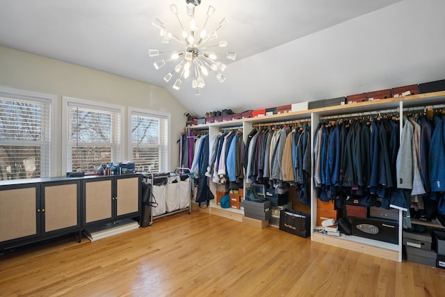 spacious closet with an inviting chandelier, lofted ceiling, and wood finished floors