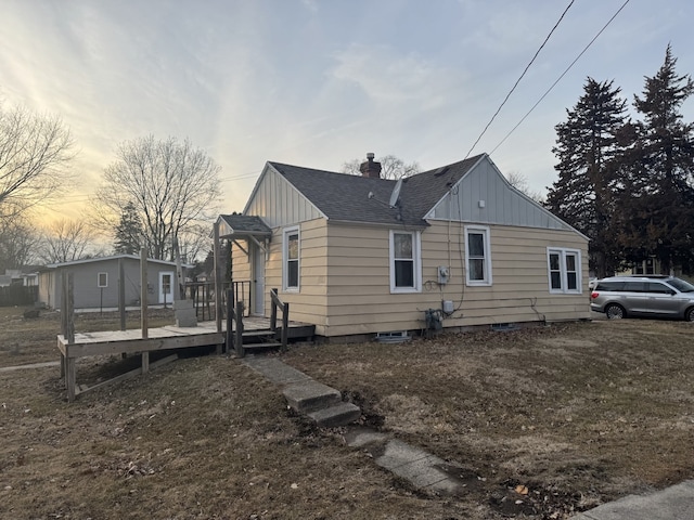 property exterior at dusk featuring a deck, a shingled roof, board and batten siding, and a chimney