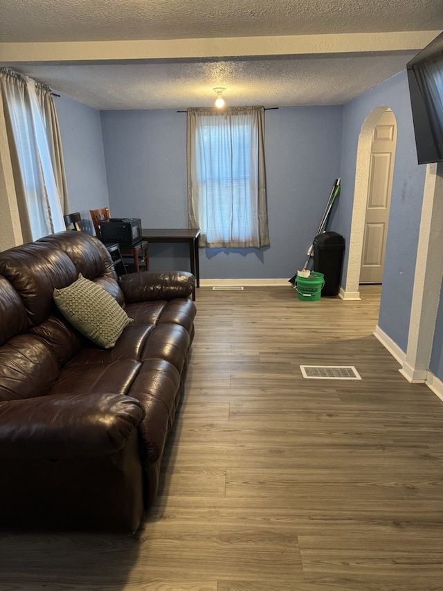 living area with arched walkways, a textured ceiling, wood finished floors, and visible vents