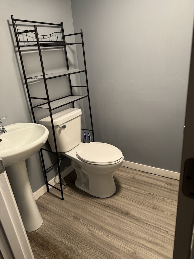 half bathroom with baseboards, toilet, and wood finished floors