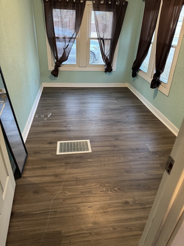 unfurnished dining area featuring a textured wall, wood finished floors, visible vents, and baseboards