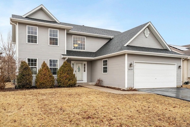 traditional home with a garage, a front yard, driveway, and a shingled roof