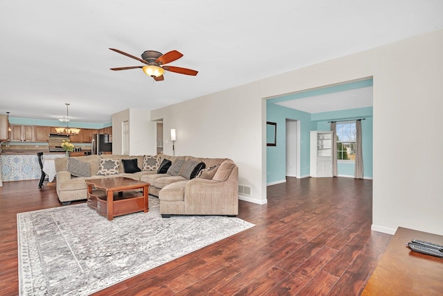 living room featuring ceiling fan with notable chandelier, dark wood-type flooring, visible vents, and baseboards