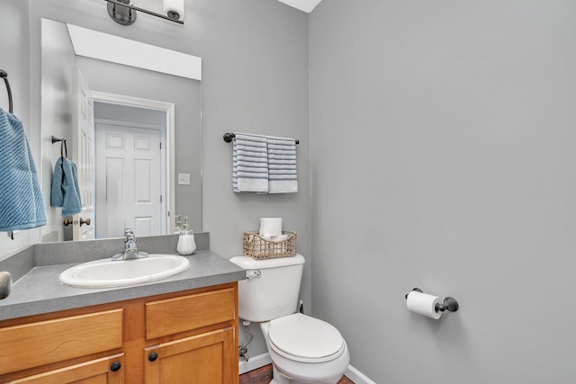 half bath with toilet, baseboards, and vanity