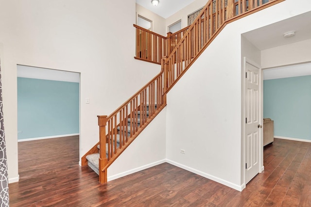 stairway featuring a towering ceiling, baseboards, and wood finished floors