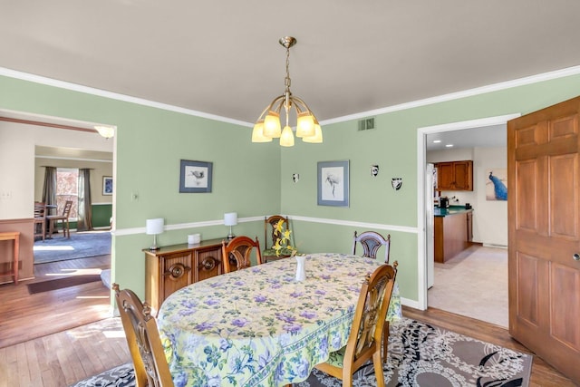 dining space with baseboards, visible vents, crown molding, light wood-type flooring, and a notable chandelier