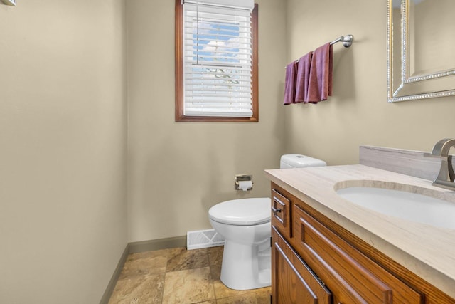 bathroom featuring toilet, vanity, visible vents, baseboards, and stone finish floor