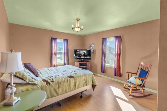 bedroom with baseboards, multiple windows, wood finished floors, and a notable chandelier