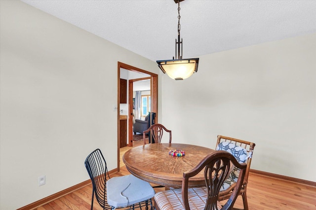 dining area featuring light wood-style floors, baseboards, and a textured ceiling