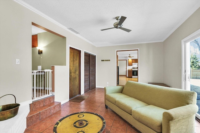 living area with tile patterned flooring, visible vents, ceiling fan, ornamental molding, and a textured ceiling