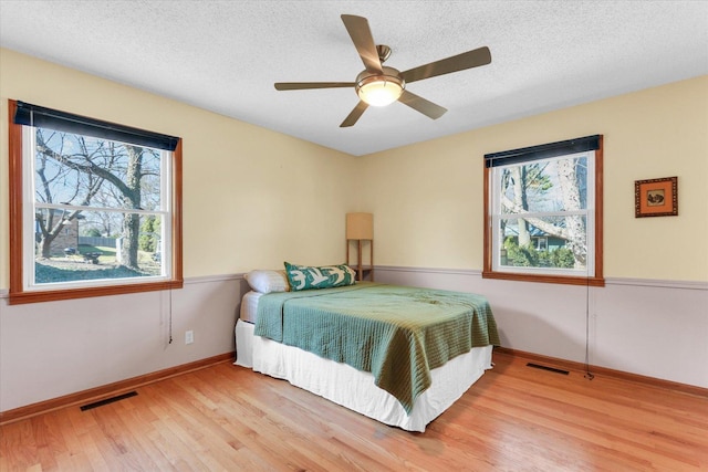 bedroom featuring visible vents, baseboards, a textured ceiling, and light wood finished floors