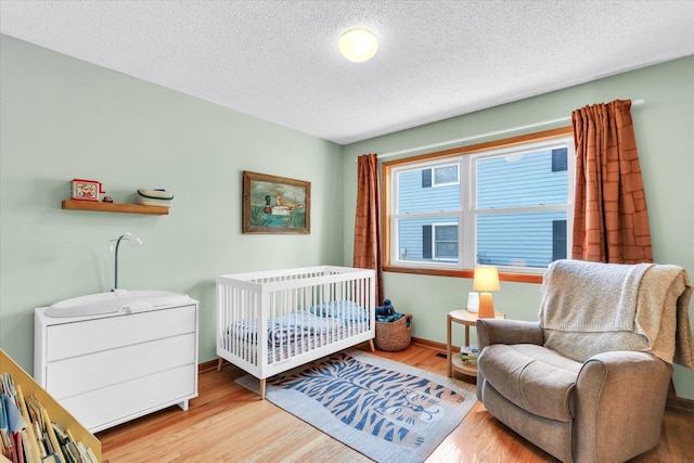 bedroom featuring a crib, wood finished floors, baseboards, and a textured ceiling