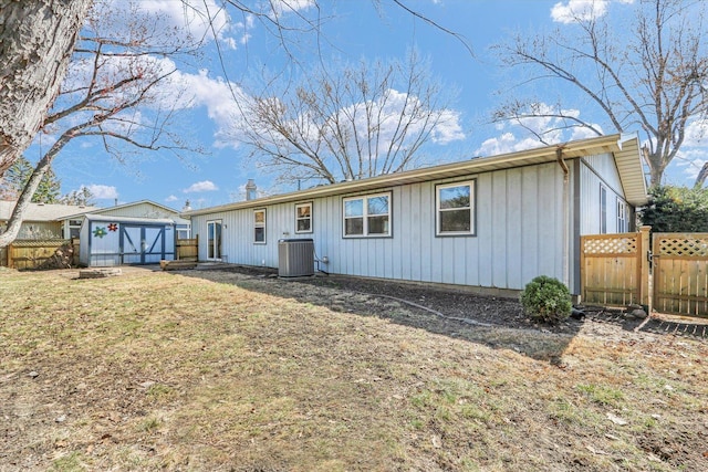 back of house featuring fence, central AC, a yard, an outbuilding, and a storage unit