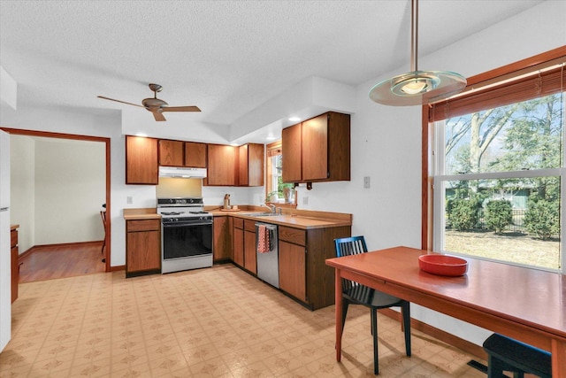 kitchen with white range with gas cooktop, brown cabinets, under cabinet range hood, light floors, and dishwasher