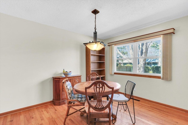 dining area with a textured ceiling, baseboards, and light wood-style floors