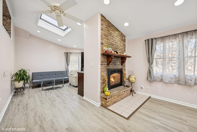 living room featuring lofted ceiling with skylight, wood finished floors, recessed lighting, baseboards, and a brick fireplace