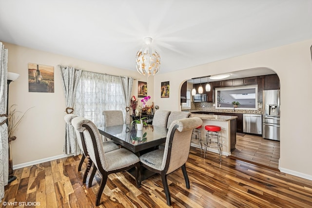 dining room featuring arched walkways, a notable chandelier, dark wood-type flooring, and baseboards