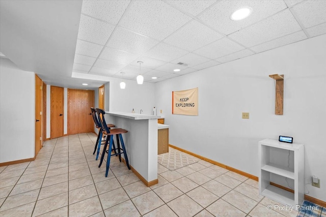 kitchen featuring light tile patterned floors, a drop ceiling, a peninsula, and a breakfast bar area