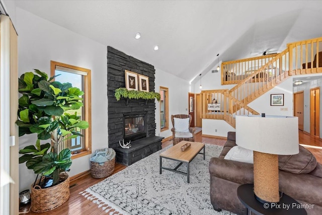 living area featuring high vaulted ceiling, a ceiling fan, wood finished floors, stairway, and a stone fireplace