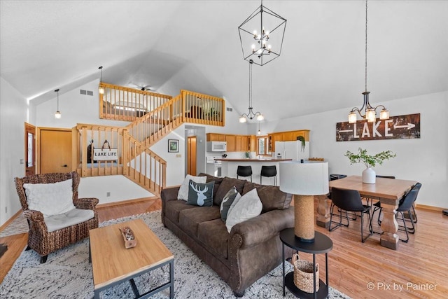 living room with visible vents, high vaulted ceiling, stairs, light wood-style floors, and a notable chandelier