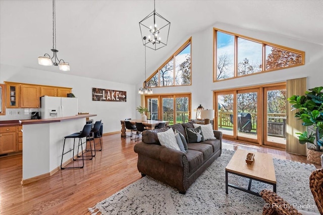 living area featuring a chandelier, light wood finished floors, high vaulted ceiling, and baseboards