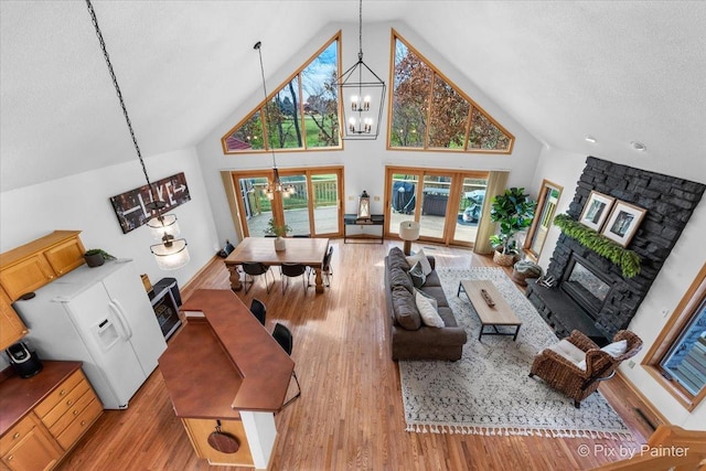 living area with a chandelier, a stone fireplace, french doors, wood finished floors, and high vaulted ceiling