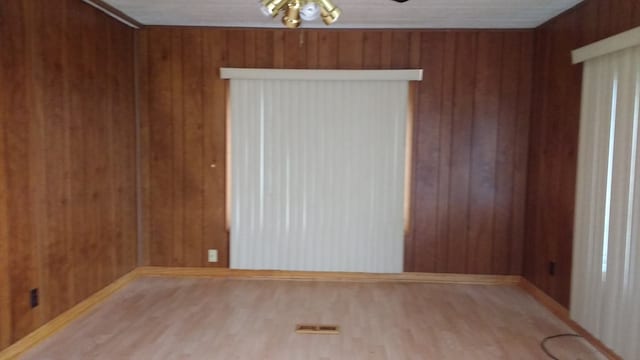 spare room featuring wood walls, a ceiling fan, visible vents, and wood finished floors