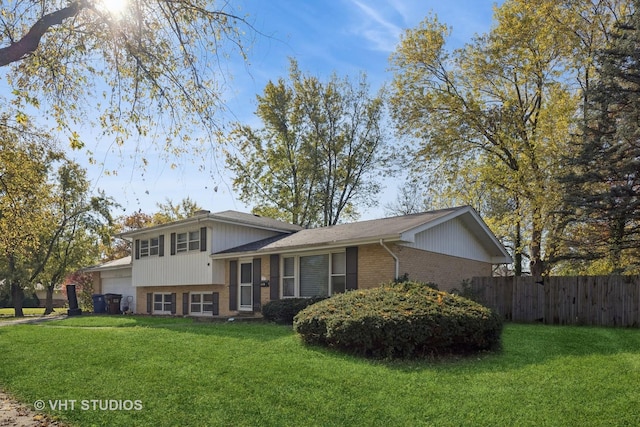 split level home featuring an attached garage, brick siding, a front yard, and fence