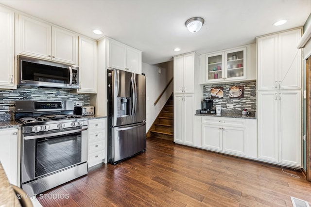 kitchen featuring stainless steel appliances, visible vents, dark wood-type flooring, white cabinets, and dark stone counters