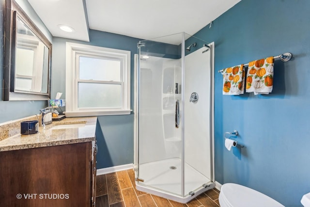 full bath featuring a stall shower, baseboards, wood finish floors, and toilet