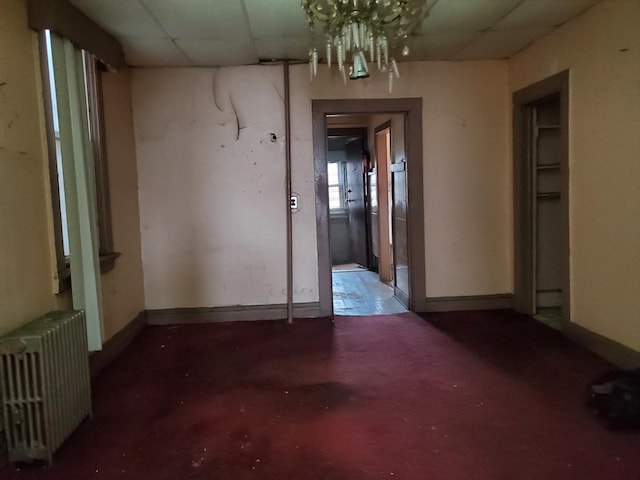 spare room featuring radiator heating unit, a paneled ceiling, baseboards, and a chandelier