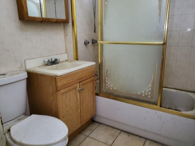 bathroom with toilet, bath / shower combo with glass door, vanity, tile walls, and tile patterned floors