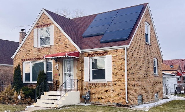 view of front of property with a shingled roof, roof mounted solar panels, and brick siding