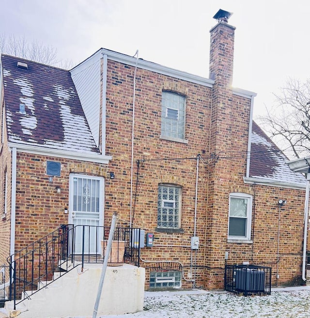 back of house with central AC, a shingled roof, a chimney, and brick siding