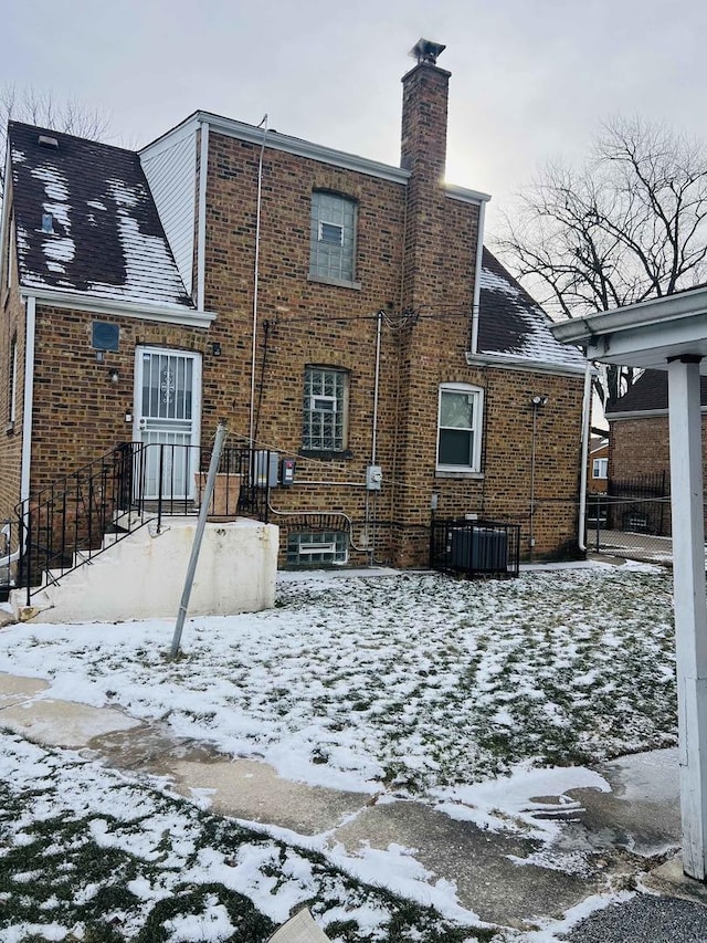 snow covered house with brick siding, a chimney, and central air condition unit