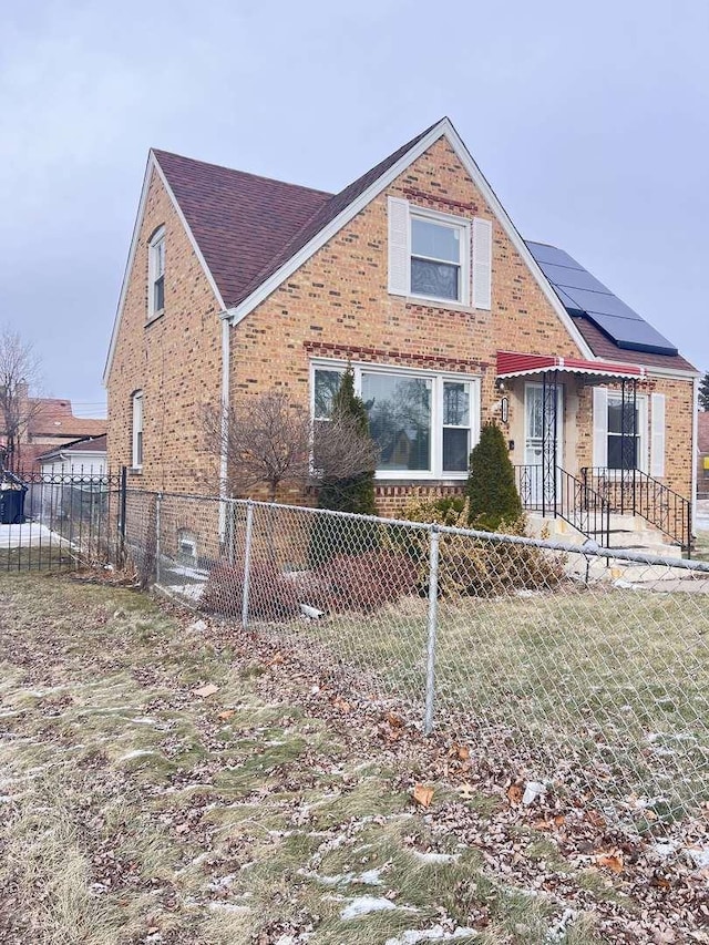 view of front facade with fence private yard, roof mounted solar panels, and brick siding