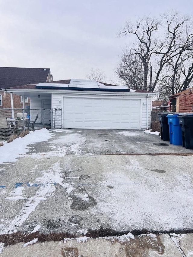 snow covered garage with solar panels, fence, and driveway