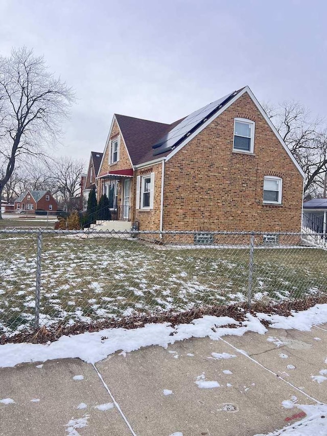 view of snowy exterior with solar panels, brick siding, and fence