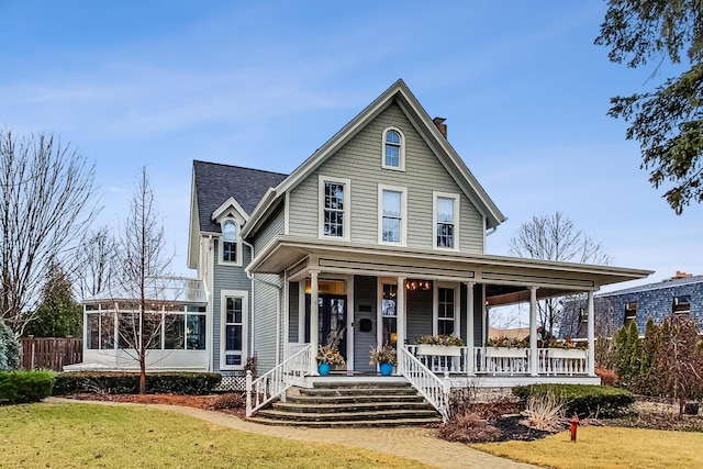 view of front of property with a chimney, covered porch, a front yard, a sunroom, and fence